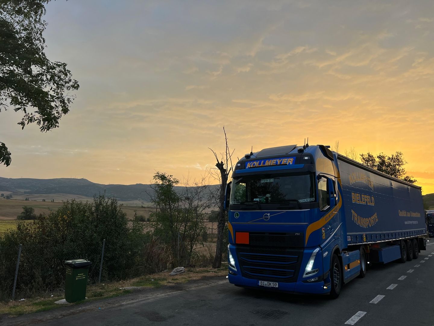 Ein LKW mit Firmenlogo fährt auf der Straße mit einem Sonnenuntergang im Hintergrund